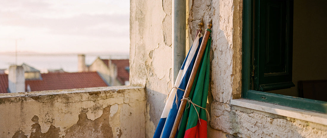 Deux drapeaux attachés à leur hampe, appuyés contre un vieux mur à Lisbonne, l'un bleu et blanc, l'autre vert et rouge, au lever du jour