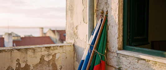 Deux drapeaux attachés à leur hampe, appuyés contre un vieux mur à Lisbonne, l'un bleu et blanc, l'autre vert et rouge, au lever du jour