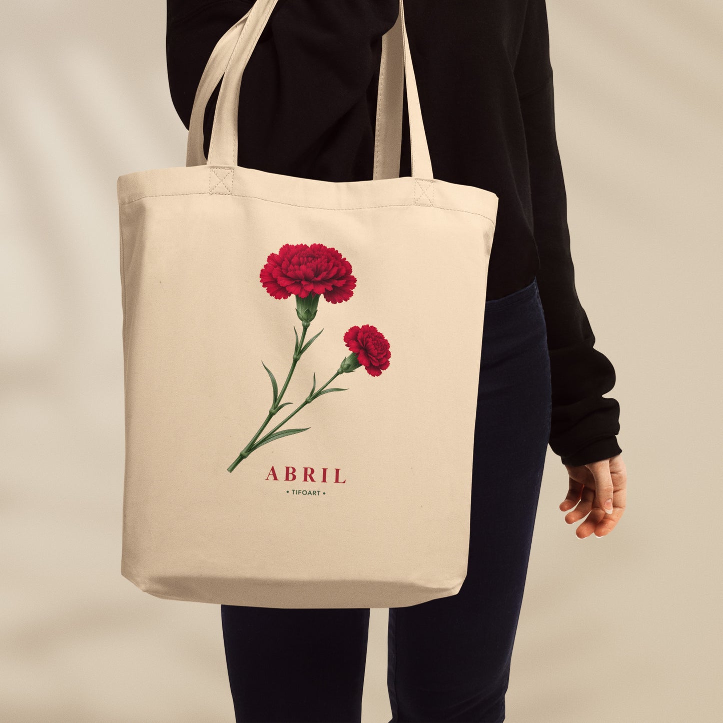 Sac tote crème porté à l'épaule, œillet rouge ouvert et bouton sur tige verte, mot Abril en serif rouge, série 25 avril Portugal TifoArt