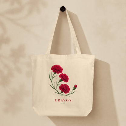 Sac tote crème oyster suspendu sur mur, bouquet d'œillets rouges et texte Cravos, série Œillets 25 avril Portugal TifoArt