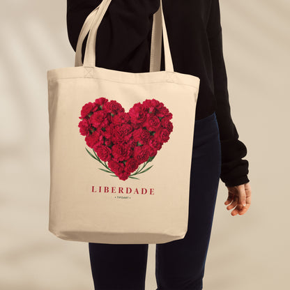 Sac tote crème porté à l'épaule, cœur d'œillets rouges et mot Liberdade en serif rouge, série 25 avril Portugal TifoArt