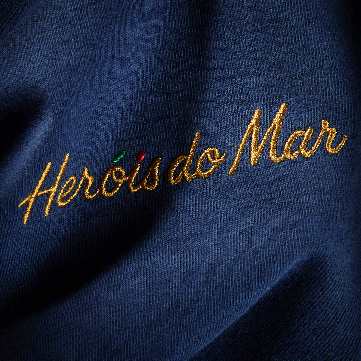 Gros plan de la broderie Heróis do Mar fil doré côté cœur sur coton Comfort Colors marine, t-shirt TifoArt