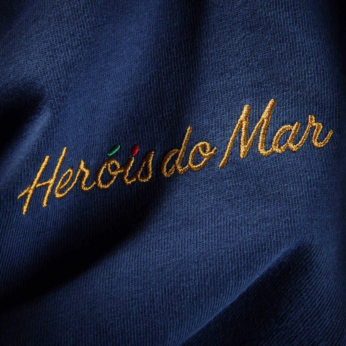 Gros plan de la broderie Heróis do Mar fil doré côté cœur sur coton Comfort Colors marine, t-shirt TifoArt