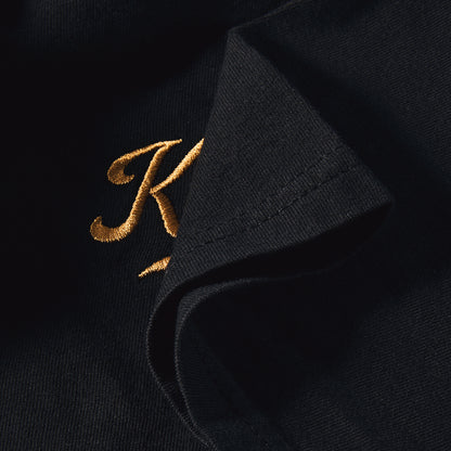 Gros plan du K brodé fil doré au pli de la manche, coton Comfort Colors noir, t-shirt Karaï TifoArt
