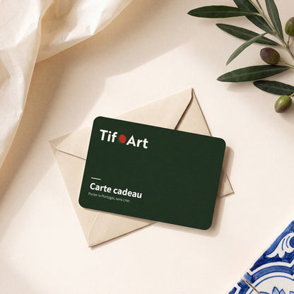 Carte cadeau TifoArt verte posée sur une enveloppe kraft, avec une branche d'olivier et un azulejo bleu et blanc